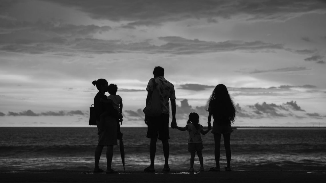 A family of five silhouetted against the ocean at sunset.