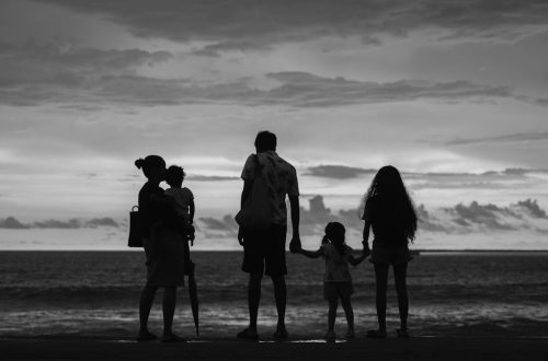 A family of five silhouetted against the ocean at sunset.