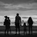 A family of five silhouetted against the ocean at sunset.